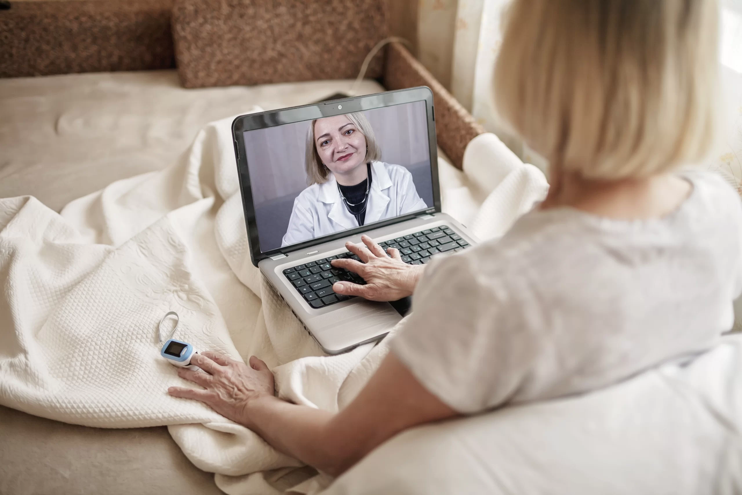 Bedridden elderly lady consulting a nurse on screen while using a connected medical device.